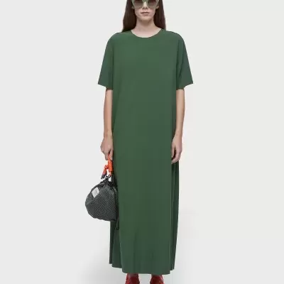 Vestido comprido verde simples com mangas curtas, bolso preto, ténis vermelho e cinzento, óculos verdes.