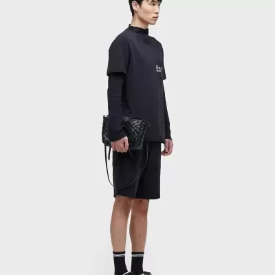 Homem de perfil com roupa preta, sapatilhas brancas e mala preta