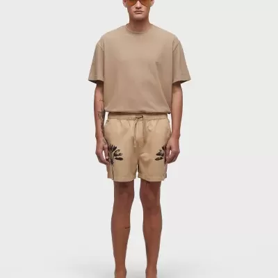 Modelo masculino com roupa casual bege e óculos de sol sobre fundo branco