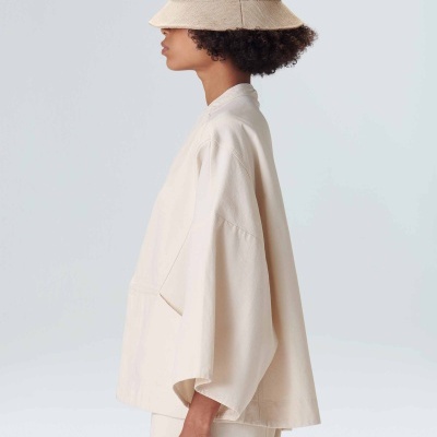 Mulher de perfil a usar chap e9u bege estilo pescador e roupa bege clara.