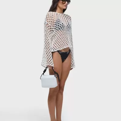Mulher com túnica branca de malha aberta, biquíni preto, óculos de sol e mala branca