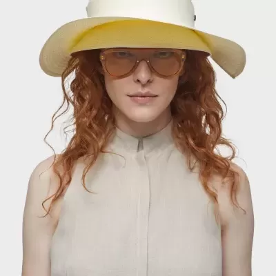 Mulher com chapéu branco e amarelo, óculos castanhos e camisa bege