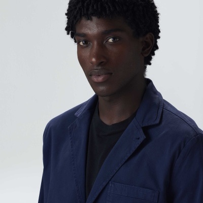 Homem com casaco azul escuro e t-shirt preta em fundo cinza claro