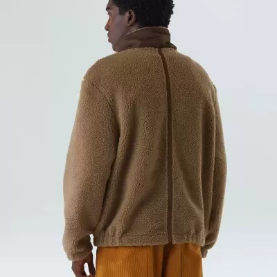 Homem de costas com casaco polar castanho e calças mostarda