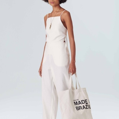 Mulher com macacão branco e sacola de pano com texto preto