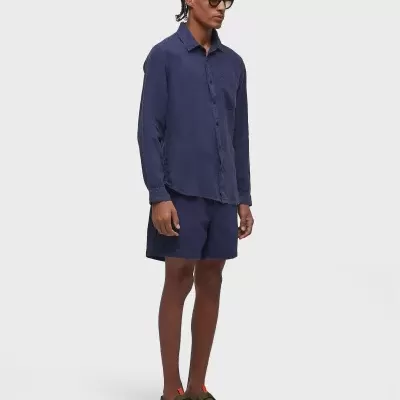 Homem com camisa e calções azuis escuros, sapatos verdes e óculos de sol pretos