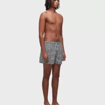 Homem jovem com calções de banho cinzentos padrão preto e branco e chinelos bege