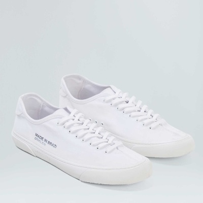 Ténis brancos em tecido com sola branca e texto 'MADE IN BRAZIL' na lateral.