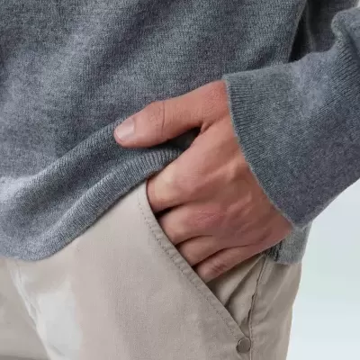 Detalhe de calças bege com mão no bolso e camisola cinzenta de malha