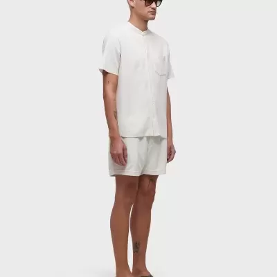 Homem com roupa branca, óculos escuros e sandálias pretas em fundo branco