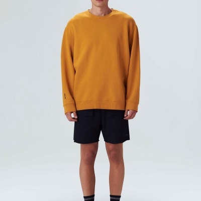 Homem com camisola amarelo mostarda e calções pretos em fundo branco