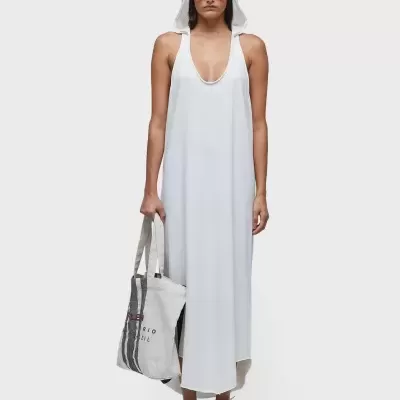 Mulher com vestido branco comprido e capuz, óculos de sol laranja, bolsa de pano e ténis brancos