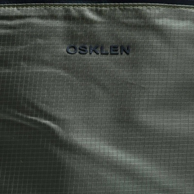 Tecido verde-oliva texturizado com padrão quadriculado e fecho de correr cinza escuro com logo OSKLEN em relevo preto
