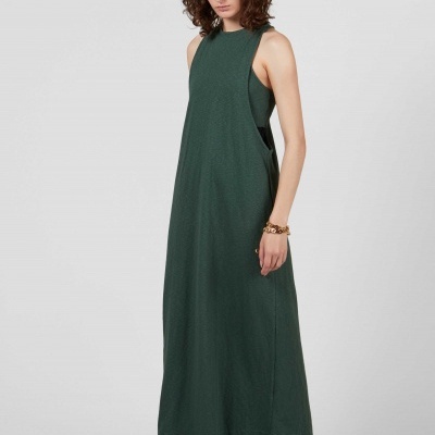 Vestido longo verde escuro em tecido liso com decote arredondado, usado por modelo com pulseira dourada e sapatos brancos baixos.