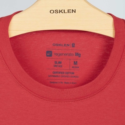 Camiseta vermelha gola redonda com etiqueta interna impressa pendurada em cabide de madeira OSKLEN