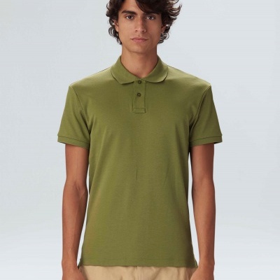 Homem vestido com polo verde de manga curta e calças bege em fundo cinza claro