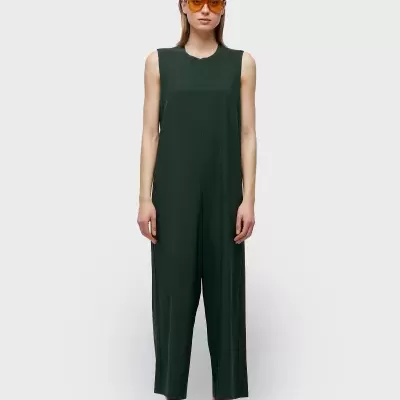 Mulher de pé a usar macacão verde escuro sem mangas e óculos de sol amarelos