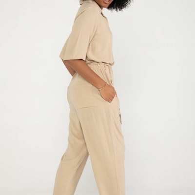 Mulher com macacão bege e sandálias creme em fundo branco