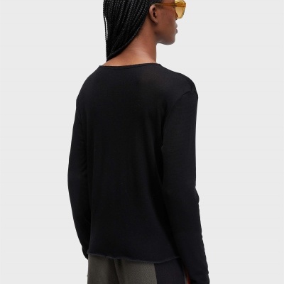 Pessoa de costas com camisa preta, calças com padrões verticais, cabelo trançado e óculos de sol amarelos.