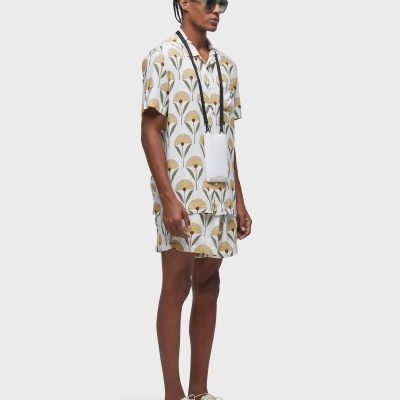 Homem com roupa estampada, calções e camisa, calçado branco e óculos escuros