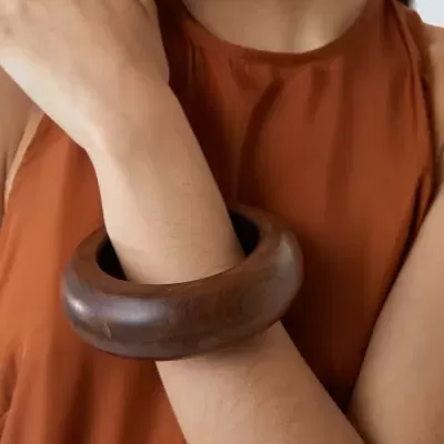 Pulseira larga de madeira castanha no pulso de mulher com blusa castanho avermelhado