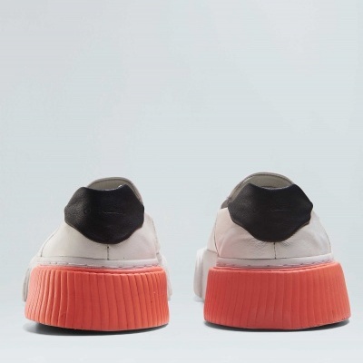 Ténis brancos com sola laranja e detalhe preto vistos de trás