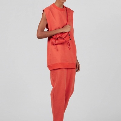 modelo veste conjunto coral com bolsa pequena e sapatos brancos em fundo cinza