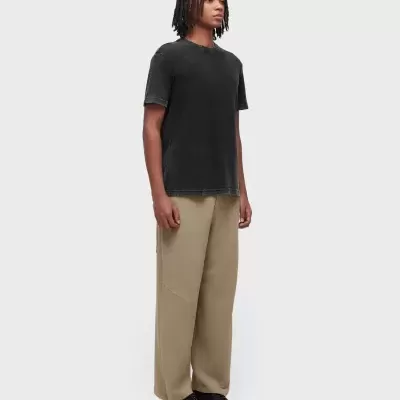 Modelo a usar camiseta preta de manga curta, calças largas bege e ténis pretos com sola branca