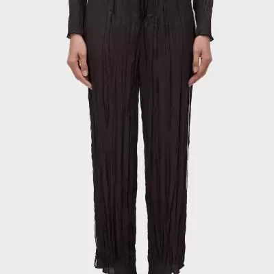 Calças pretas com textura vincada e sandálias castanhas em fundo cinza