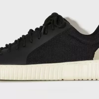 Tênis desportivo preto com sola branca e reforço bege no calcanhar