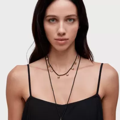 Mulher com vestido preto e dois colares pretos com detalhes dourados.
