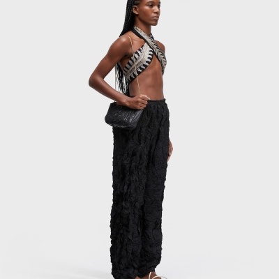 Modelo de vestido com top assimétrico, calças largas pretas, sandálias brancas e bolsa preta com alça dourada