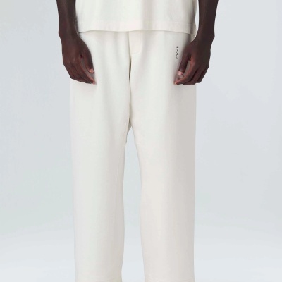 Calças desportivas creme em tecido macio, corte largo, com ténis creme.