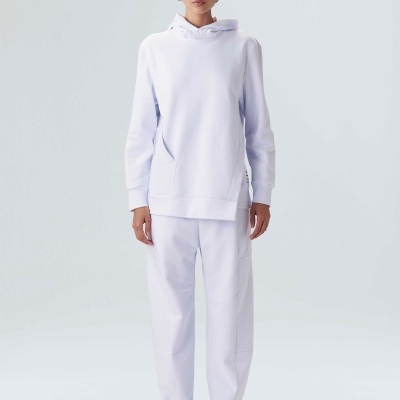 Mulher com conjunto desportivo branco com hoodie e calças largas, calça sapatilhas brancas, fundo cinzento