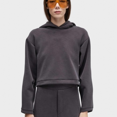 Mulher com sweatshirt cinza escuro com capuz, calças cinza e óculos de sol âmbar.