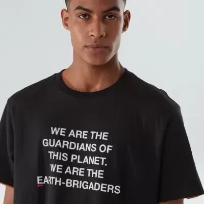 Modelo masculino a usar t-shirt preta com texto branco sobre proteção do planeta.