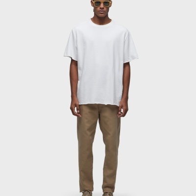 Modelo com t-shirt branca, calças castanhas e sapatilhas bege em fundo branco