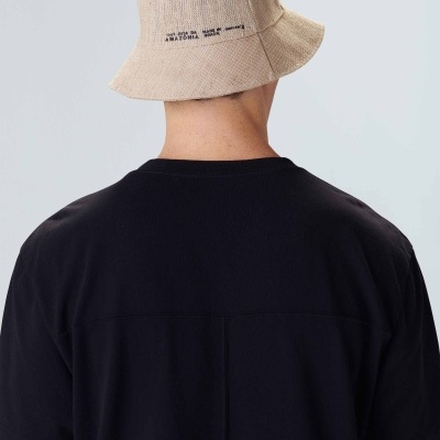 Chapéu tipo pescador bege com texto na parte traseira usado por pessoa de costas vestindo t-shirt preta