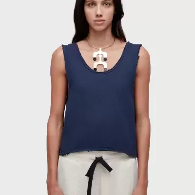 Mulher com top azul e calças claras com cordão preto e um colar metálico grande