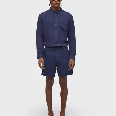 Homem a usar camisa azul escura de manga comprida e calções azuis escuros com óculos de sol e sandálias