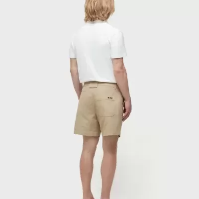 Homem de costas com camisa branca, calças curtas bege e chinelos pretos