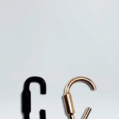 Dois mosquetões metálicos, um preto e um dourado, sobre superfície cinzenta