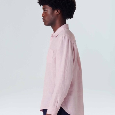 Homem com camisa rosa de manga comprida e calças escuras, vista lateral