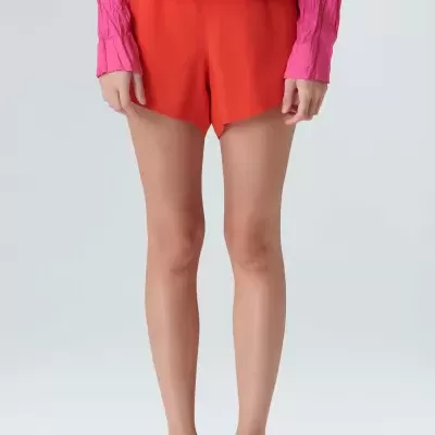 Calções vermelhos lisos usados por mulher com camisa rosa e sandálias brancas