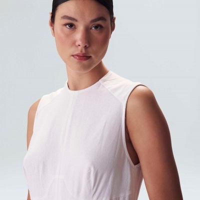 Mulher com vestido branco sem mangas e cabelo apanhado em fundo claro