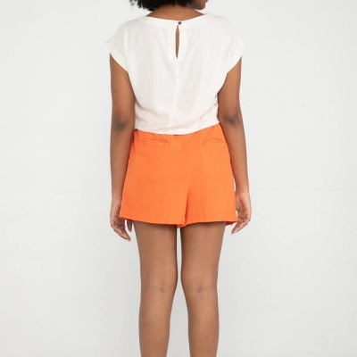 Mulher vestindo blusa branca e calções laranja, vista de costas.