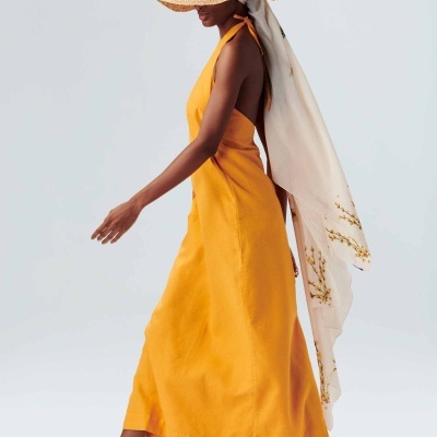 Mulher de lado com vestido amarelo longo, chapéu de palha e sandálias