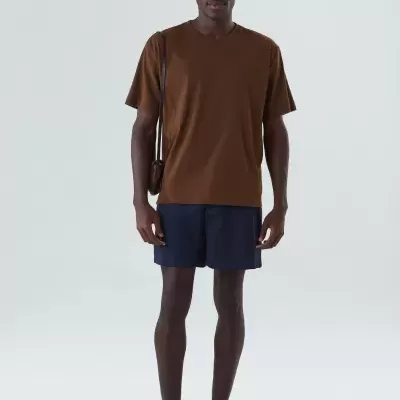 Homem vestido com roupa casual castanha e azul, em fundo branco.