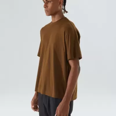 Homem com t-shirt castanha de manga curta e calças pretas em fundo branco