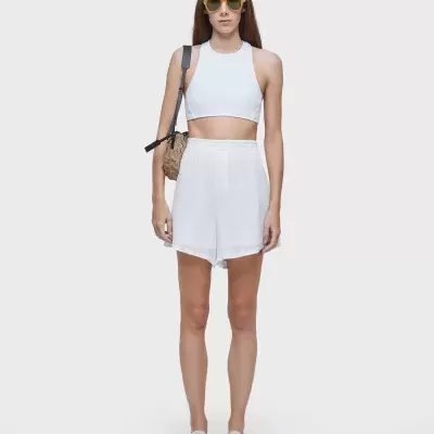 Mulher com top branco, calções brancos, óculos amarelos e mochila castanha